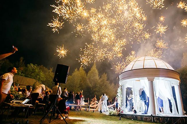 Fireworks explode in the night sky above an outdoor wedding.