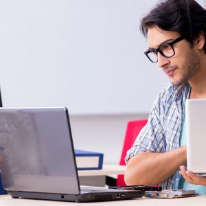 IT Foundations Bundle image of young man in black framed glasses reading from laptop on desk in classroom