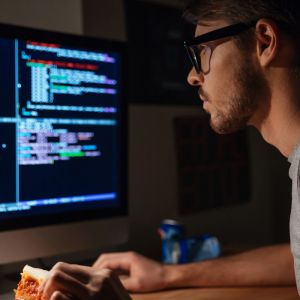 Java Programmer image of young man wearing glasses looking at computer screen of colorful coding on black background