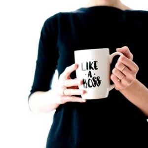 A woman in a black turtleneck holds a cup in her hands that reads "Like a Boss".